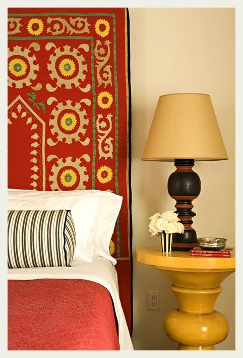 a bedroom with a red headboard and yellow night stand next to a lamp on a small table