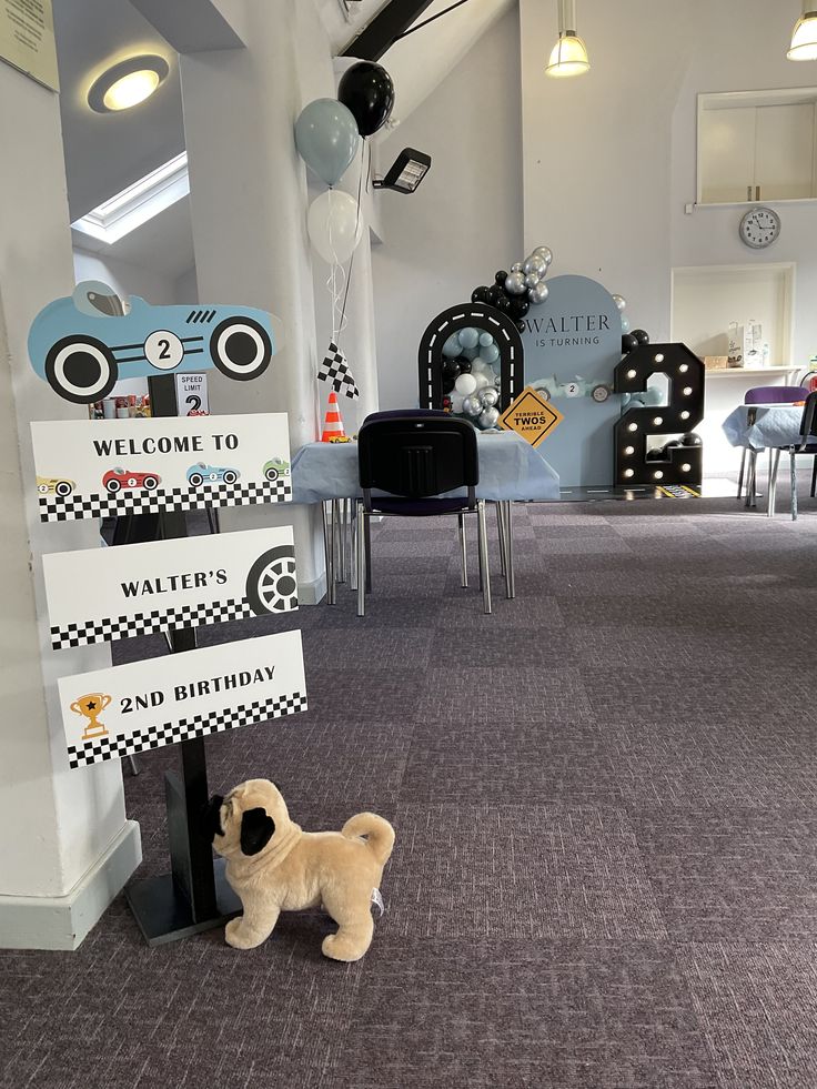 a stuffed dog standing next to a welcome sign in a room with chairs and balloons