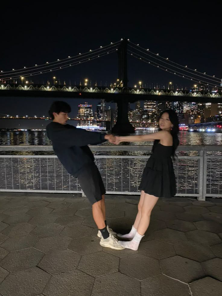 two people standing on their legs in front of the water with a bridge in the background