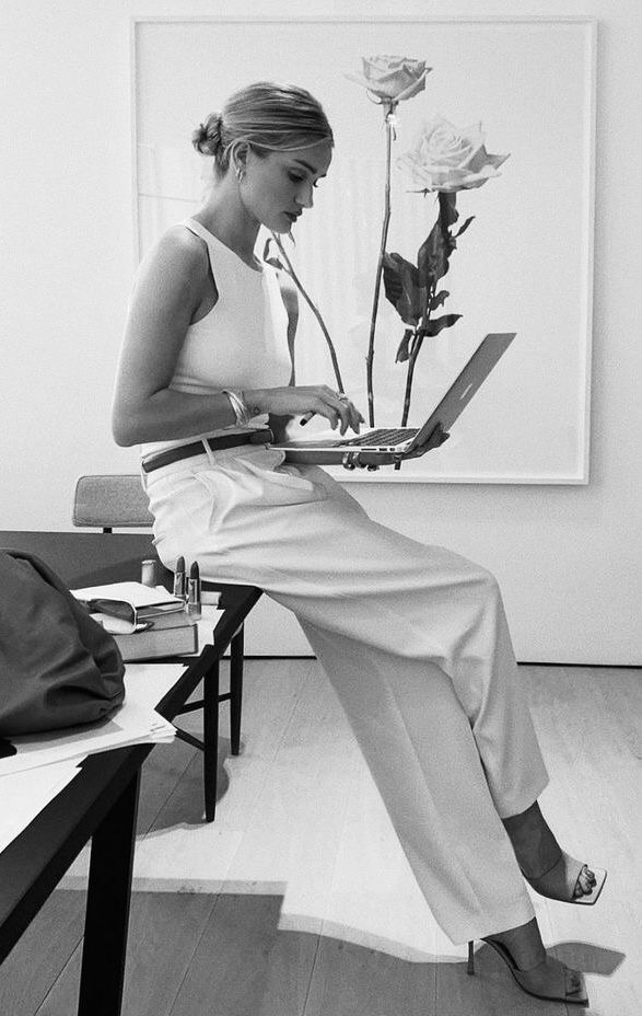 a woman sitting on a bench with a laptop in front of her and a rose behind her