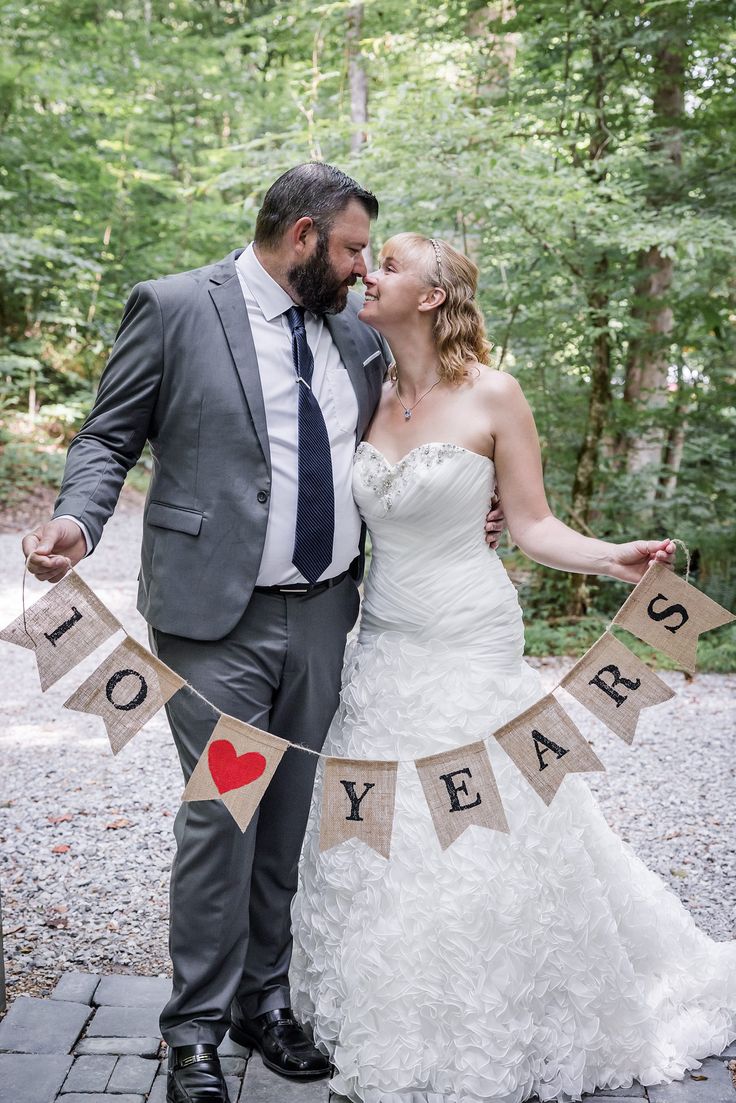 a bride and groom standing next to each other in front of some trees with bunting