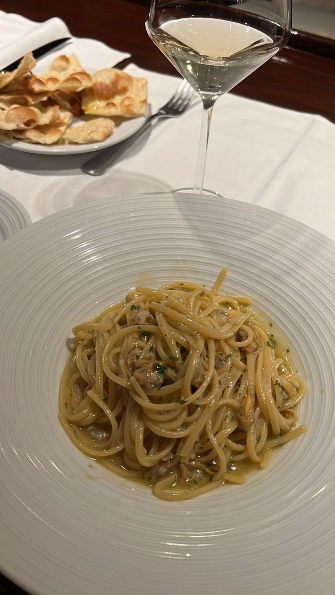 a white plate topped with pasta next to a glass of wine