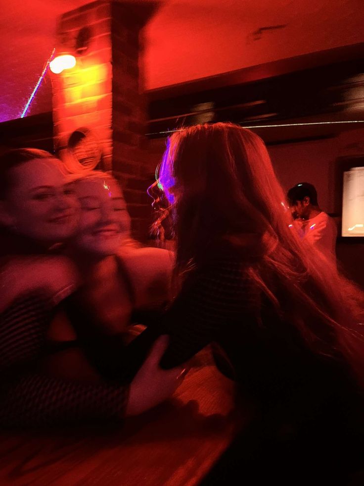 two women hugging each other in a bar with red lights on the wall behind them