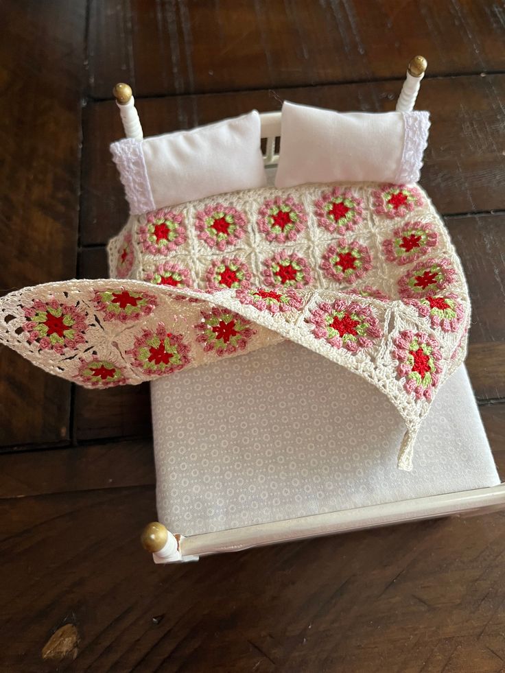 a doll's crocheted bed with pink flowers and white sheets on it