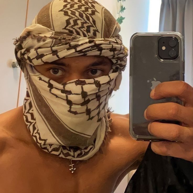 a shirtless man wearing a bandana taking a selfie with his cell phone