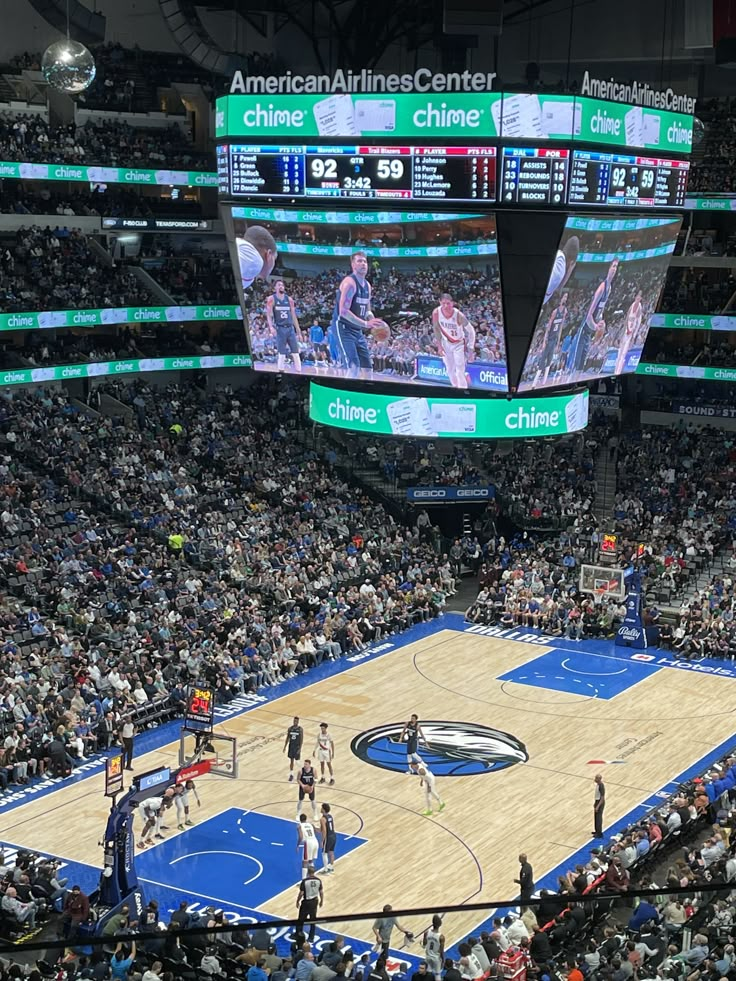 an arena filled with lots of people watching a basketball game on the big screen tv