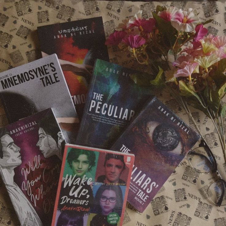 there are many books on the bed next to some flowers and reading utensils