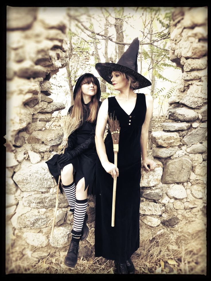 two women dressed up as witches standing next to each other in front of a stone wall