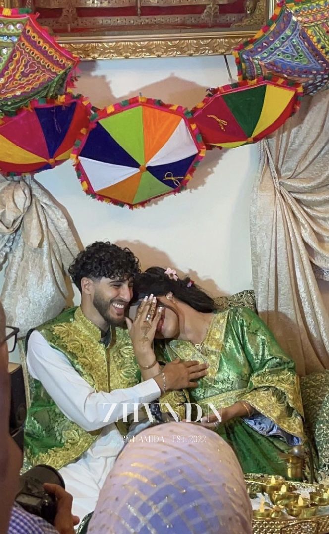 a man and woman sitting on top of a bed covered in colorful umbrellas next to each other