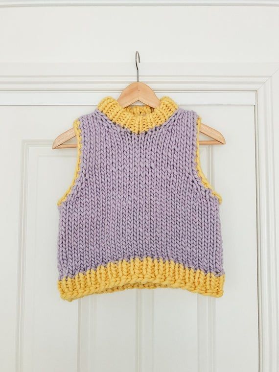 a purple and yellow knitted sweater hanging on a white door frame with a wooden hanger