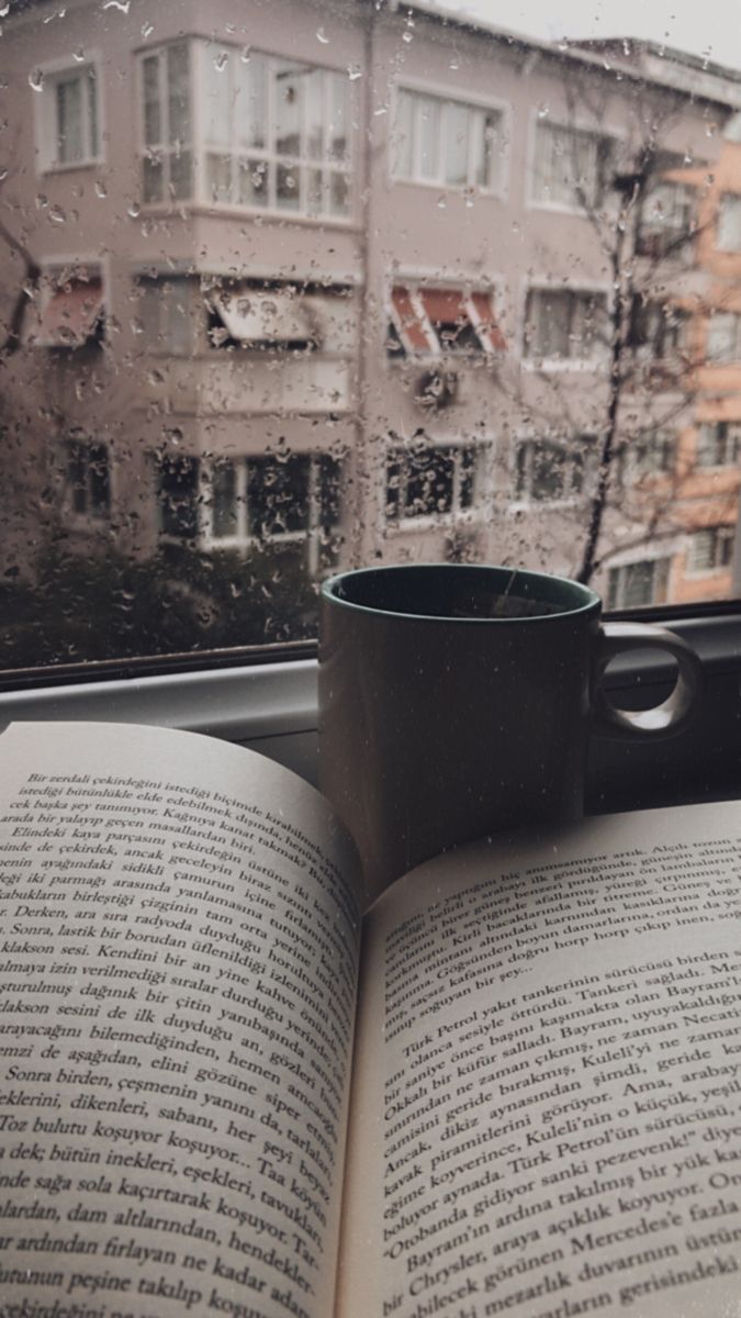 an open book sitting on top of a window sill next to a coffee cup