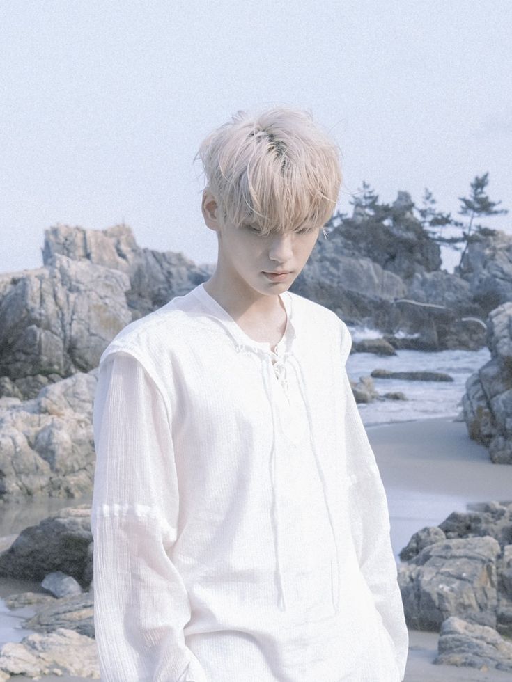 a young man standing on top of a beach next to rocks and water with trees in the background