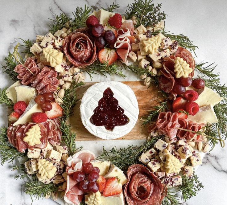 a wreath made out of cheese, meats and fruit on a marble counter top