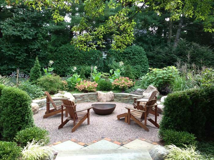 an outdoor seating area with chairs and fire pit surrounded by greenery, shrubs and trees