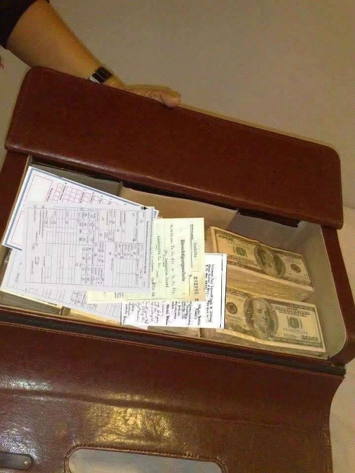 a suitcase filled with lots of money sitting on top of a floor next to a wall