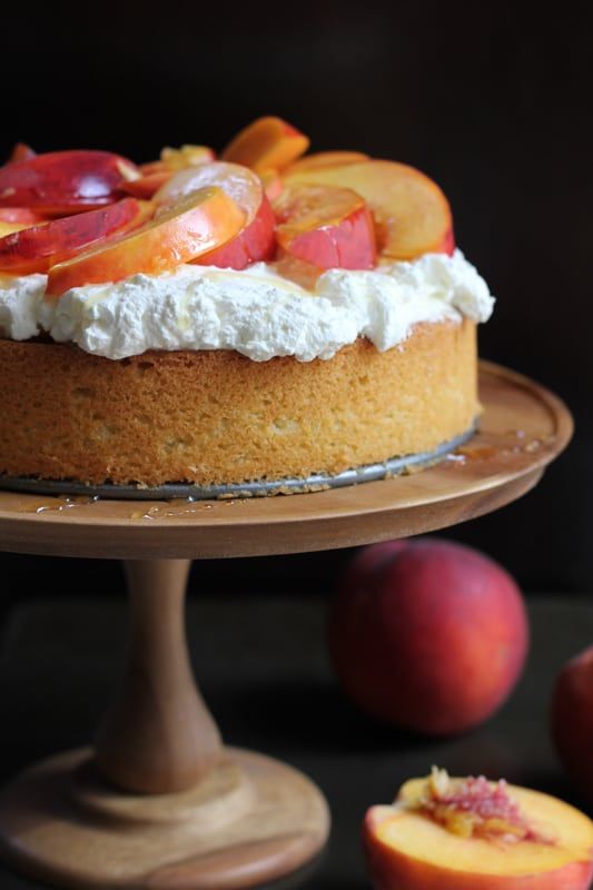 there is a cake with peaches and whipped cream on the top, next to some fruit