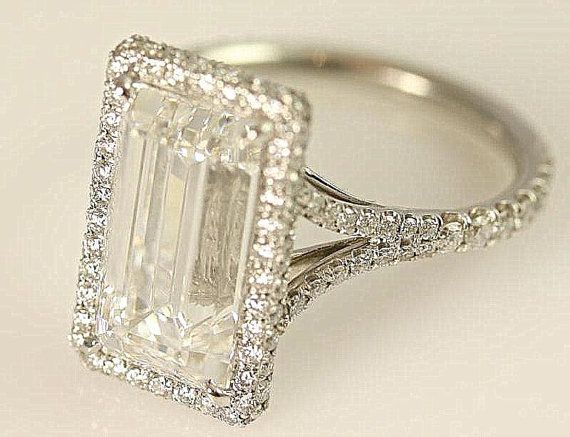 an emerald cut diamond ring with pave set diamonds around the band and shoulders, on a white background