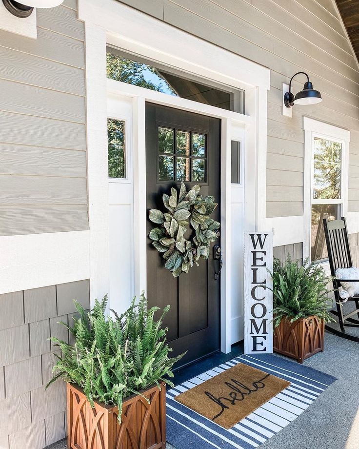 a welcome sign on the front door of a house with potted plants and chairs