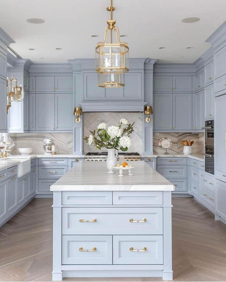 a kitchen with blue cabinets and white counter tops, gold accents on the chandelier