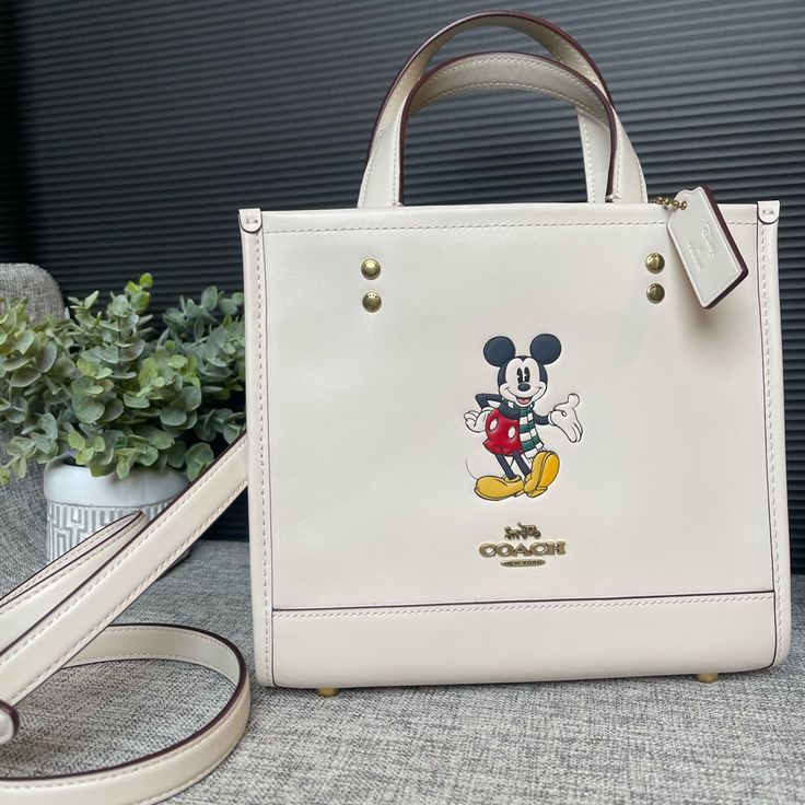 Coach Disney X Coach Dempsey Tote 22 With Mickey Mouse Leather Chalk.Inside Zip And Multifunction Pockets.Snap Closure, Fabric Lining. For Protective Feet At Base. Refined Calf Leather.Detachable Strap With 22 1/2” Drop For Shoulder Or Crossbody Wear.Handle With 4 1/4” Drop. 8 3/4”(L) 7 3/4(H) 4 1/4”(W) Coach Dempsey Tote 22, Coach Dempsey Tote, Coach X Disney, Coach Zip Top Tote, Coach Disney, Plaid Tote, Mouse Color, Coach Tote Bags, Satchel Tote Bag