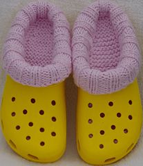 a pair of yellow and pink crocheted shoes on a white surface with holes in the soles