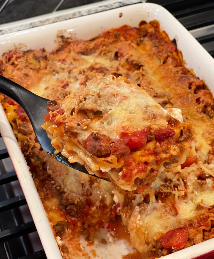 a casserole dish with meat, cheese and sauce in it is being lifted by a spatula