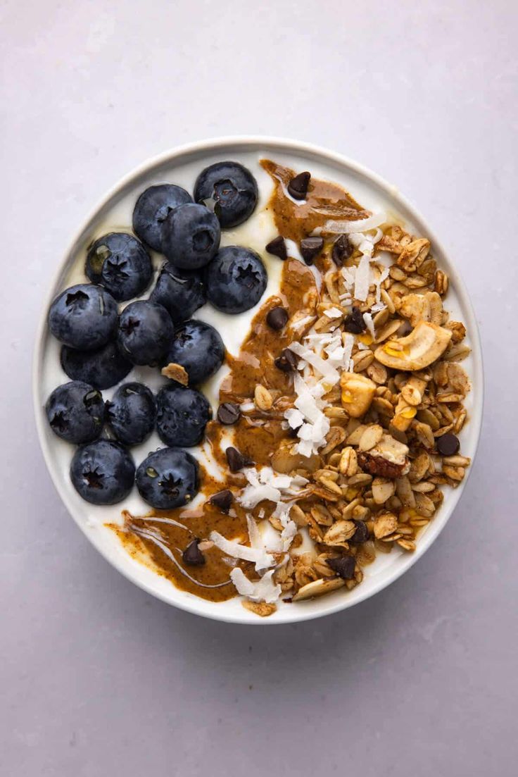 blueberries, granola and yogurt in a bowl on a white surface