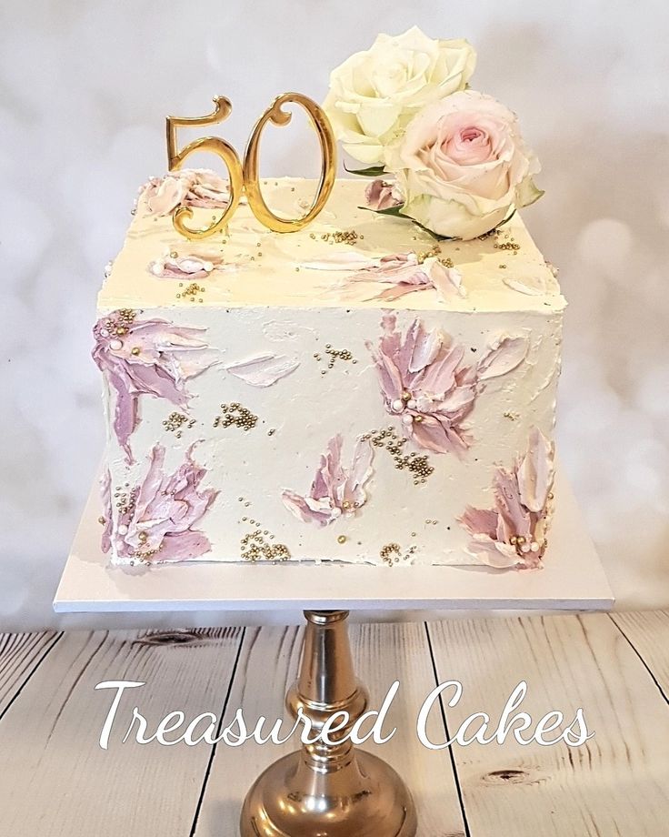 a white cake with pink flowers and gold number 50 on top, sitting on a wooden table