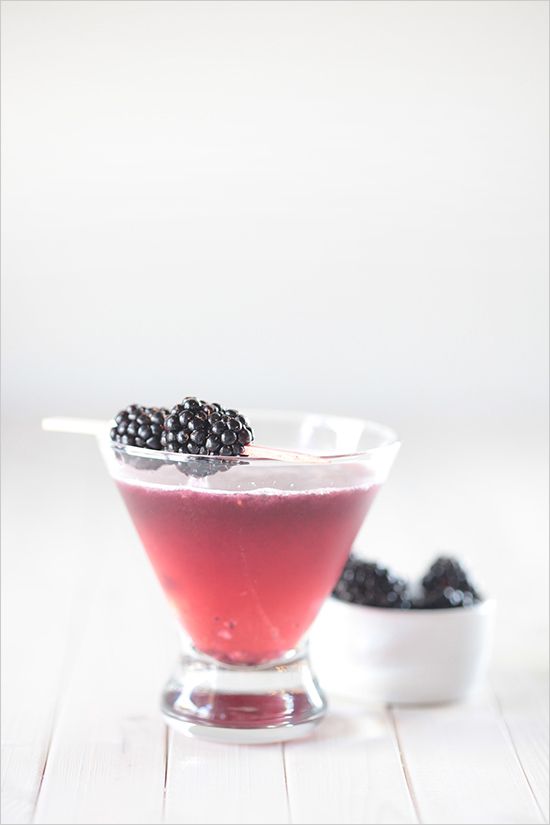 a glass bowl filled with berries on top of a white wooden table next to a spoon