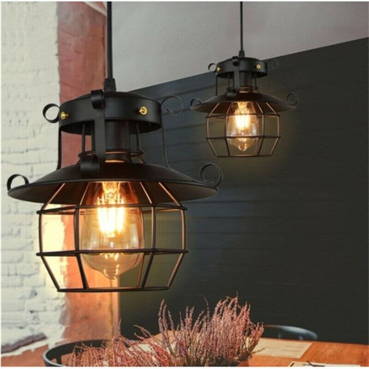 two light fixtures hanging from the ceiling over a wooden table with plants and flowers on it