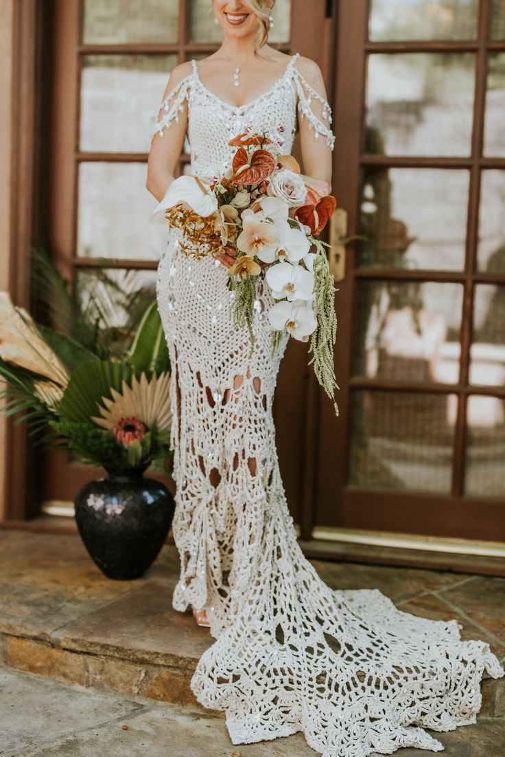 a woman standing in front of a door holding a bouquet of flowers and greenery