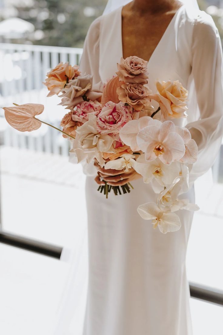 a woman holding a bouquet of flowers in her hand and wearing a white dress with long sleeves