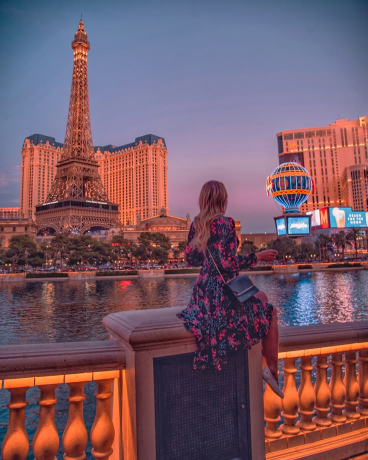 a woman is sitting on a ledge looking at the eiffel tower in paris