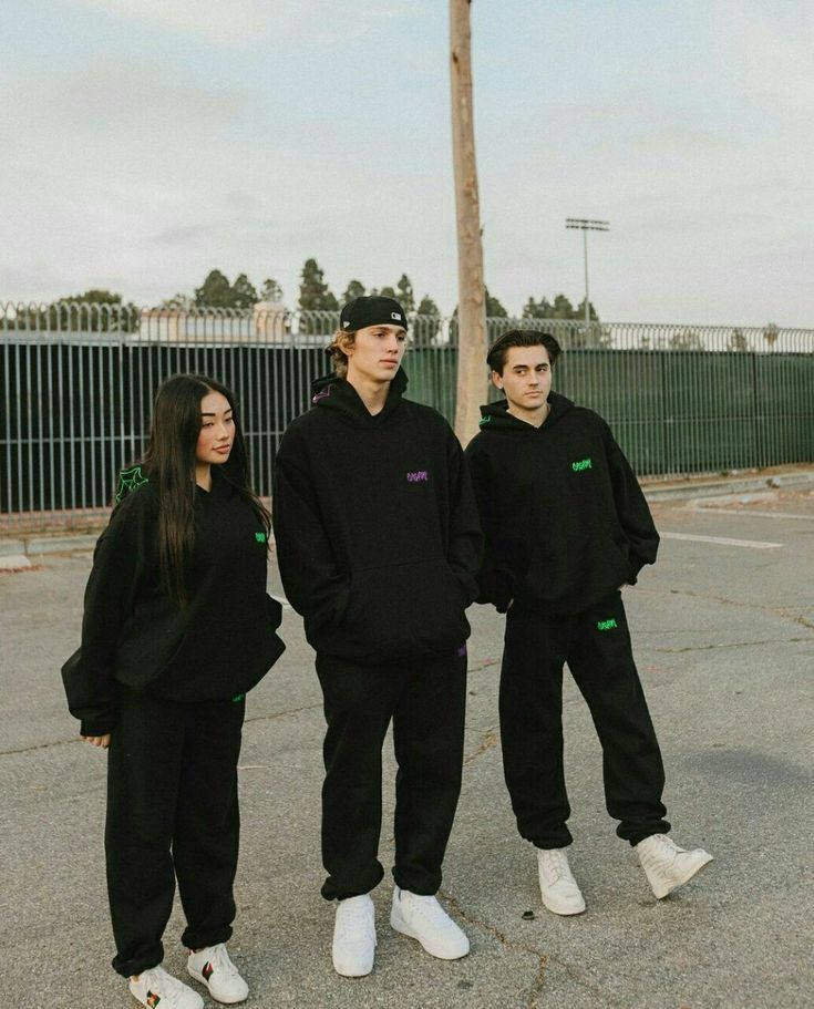 three people standing in the middle of an empty parking lot, one wearing a black hoodie