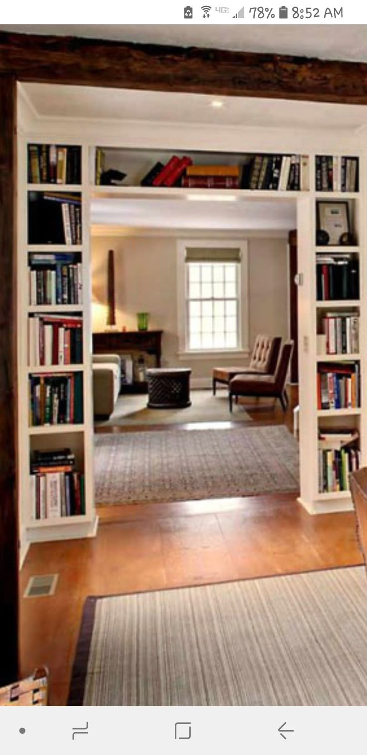 a living room filled with furniture and bookshelves next to a doorway that leads to a sitting area