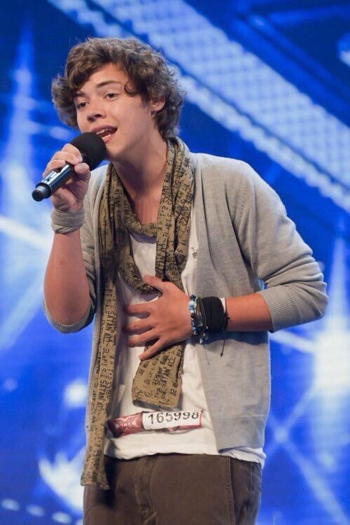 a young man holding a microphone in his right hand and wearing a scarf around his neck