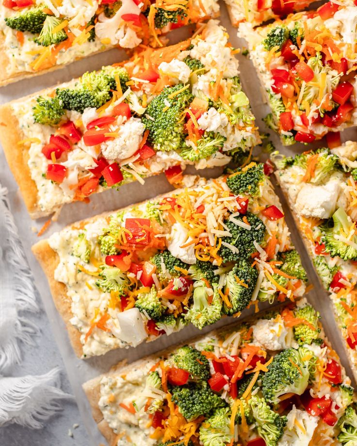 several slices of pizza with broccoli, cheese and tomatoes on them sitting on a sheet of parchment paper