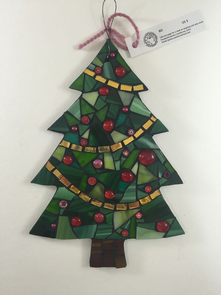 a stained glass christmas tree ornament hanging on a wall with a red ribbon