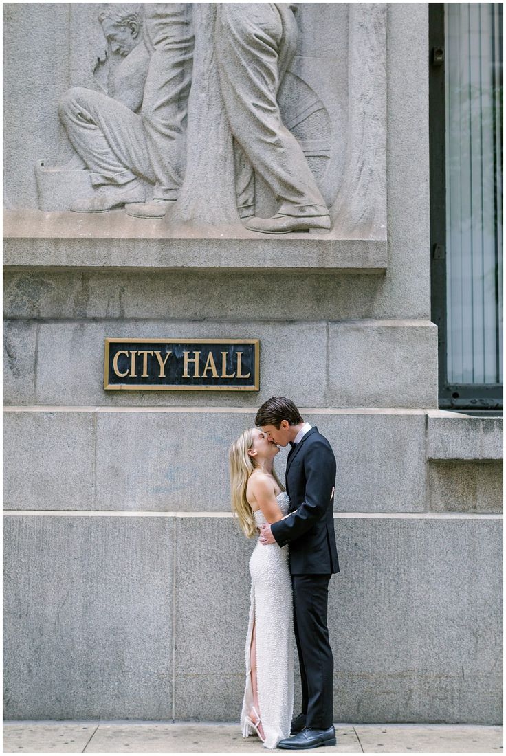 a man and woman standing in front of a statue with the words city hall written on it