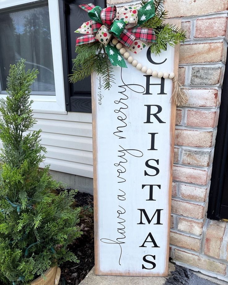 a wooden sign that says merry christmas and is decorated with evergreens, pine cones and burlocks