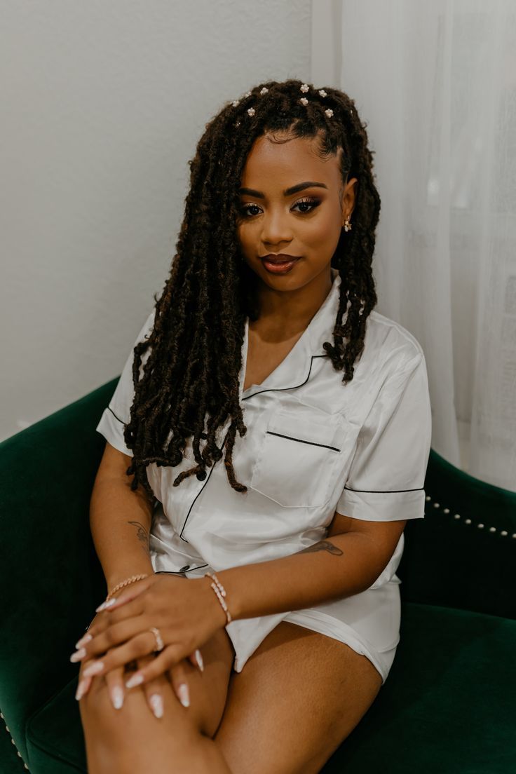 a woman sitting on top of a green chair with her legs crossed and wearing white