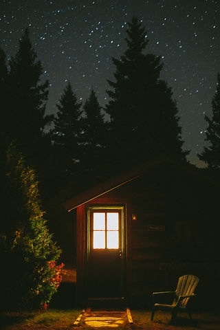 a cabin in the woods at night with stars above it and a lawn chair on the grass