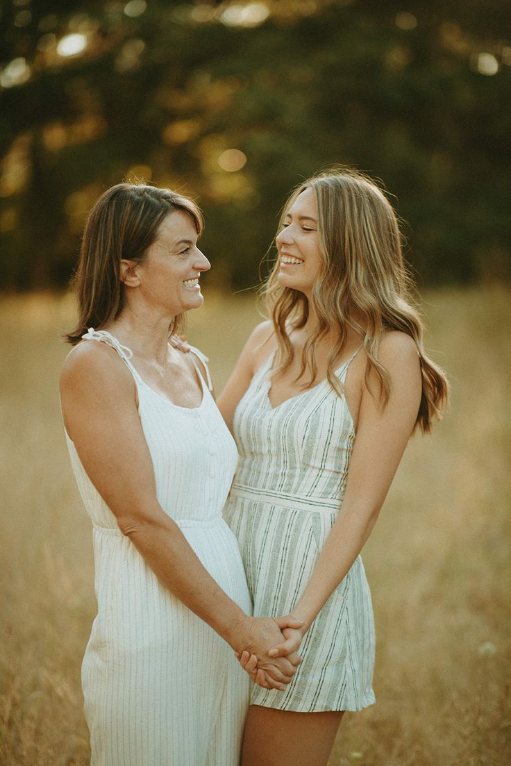 two beautiful women standing next to each other in the middle of a field smiling at each other