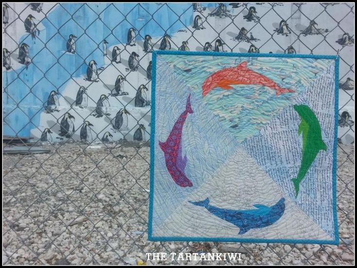 there is a quilt on the ground next to a chain link fence with several penguins