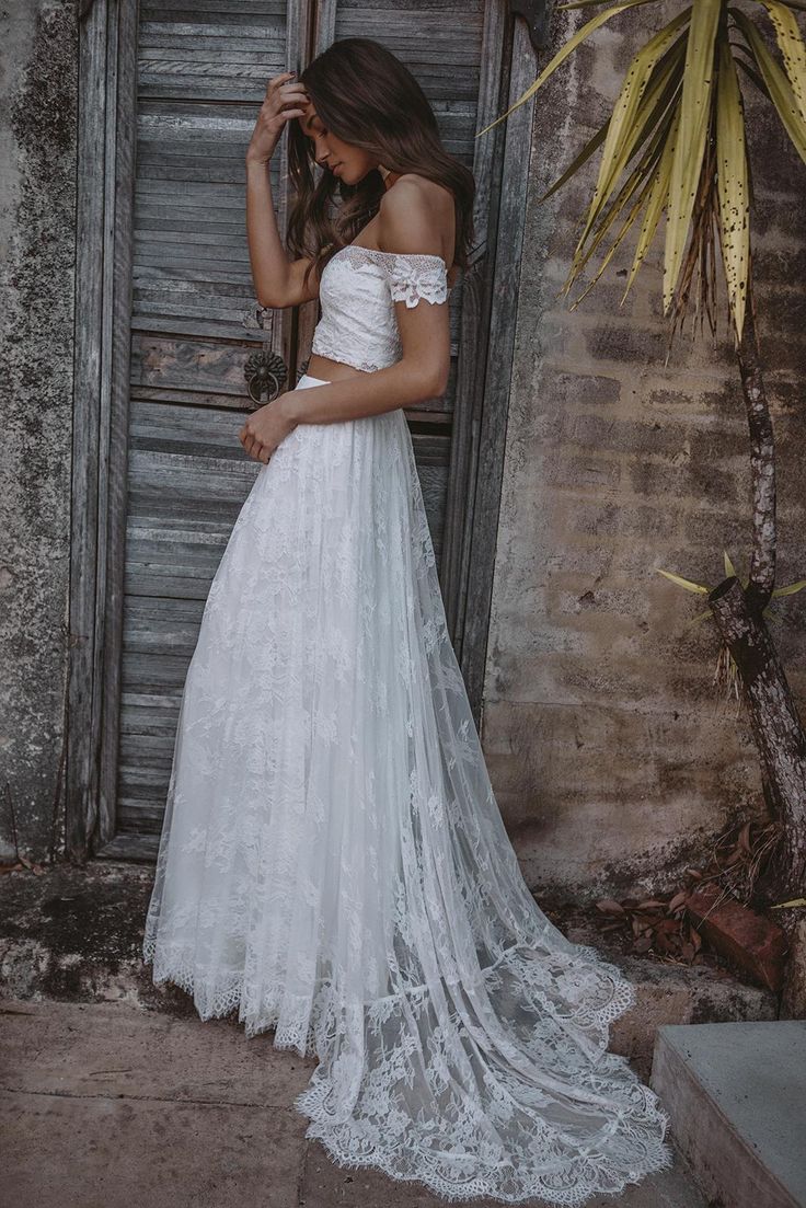 a woman standing in front of an open door wearing a white wedding dress with off the shoulder sleeves