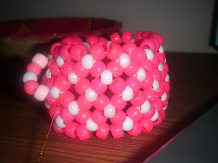 a pink and white beaded bracelet sitting on top of a wooden table