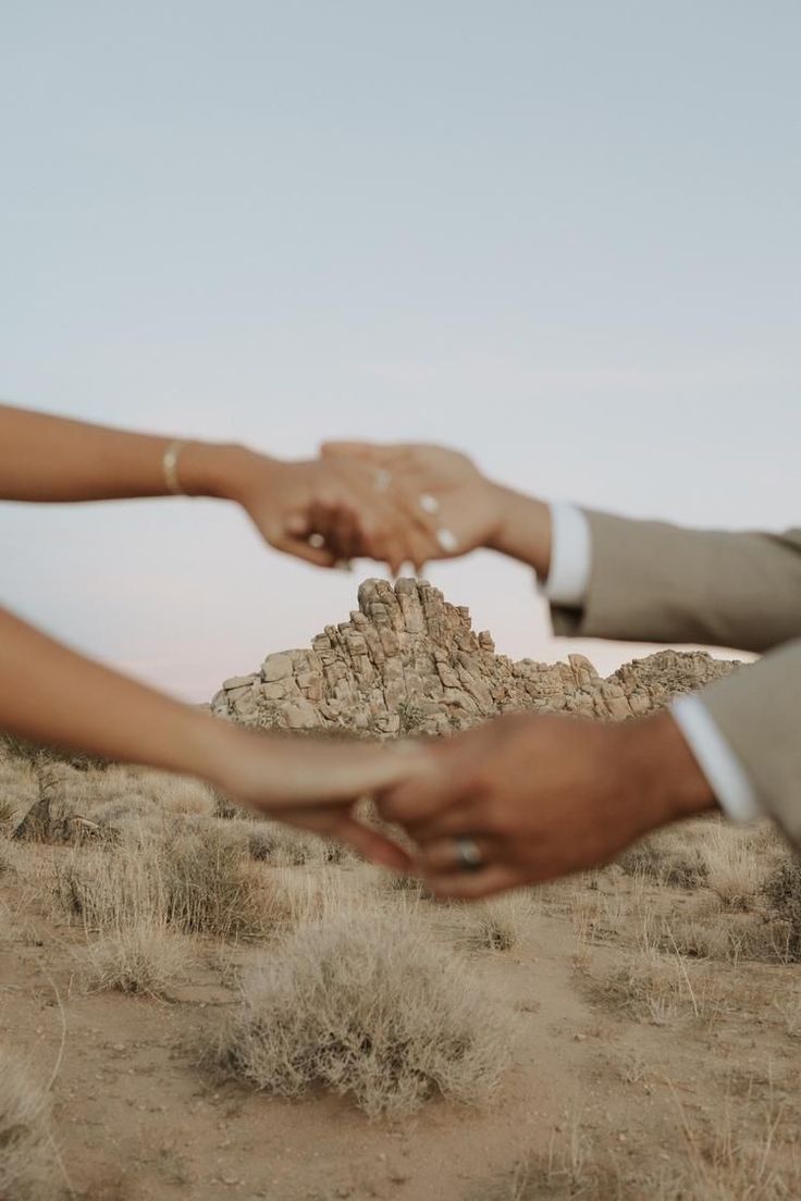 two people reaching out their hands to touch each other's hand in the desert