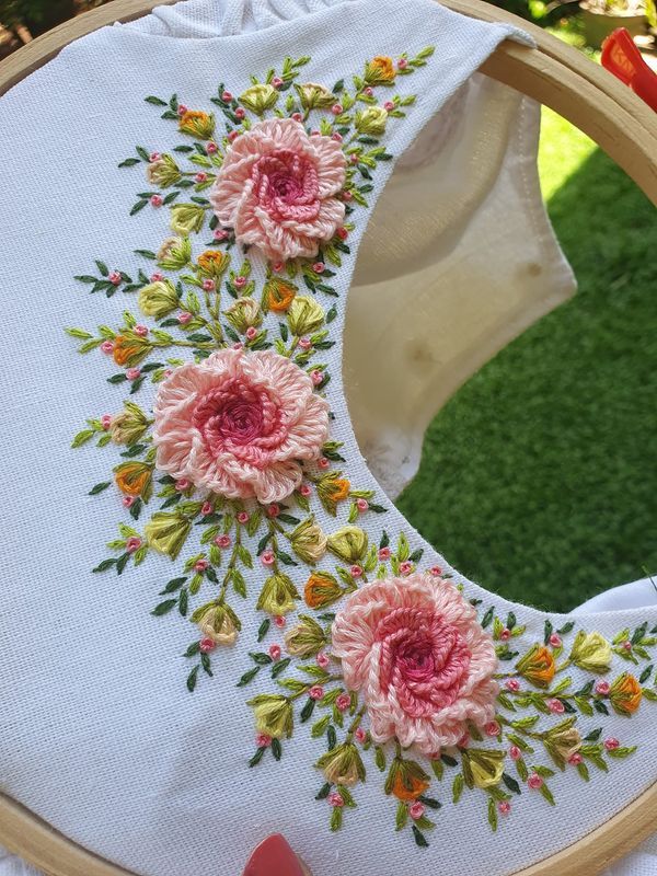 a close up of a embroidery on a hoop with flowers in the center and green grass behind it