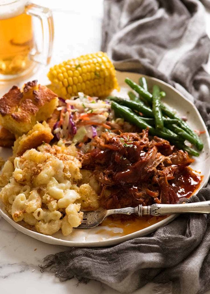 a white plate topped with meat, potatoes and green beans next to corn on the cob