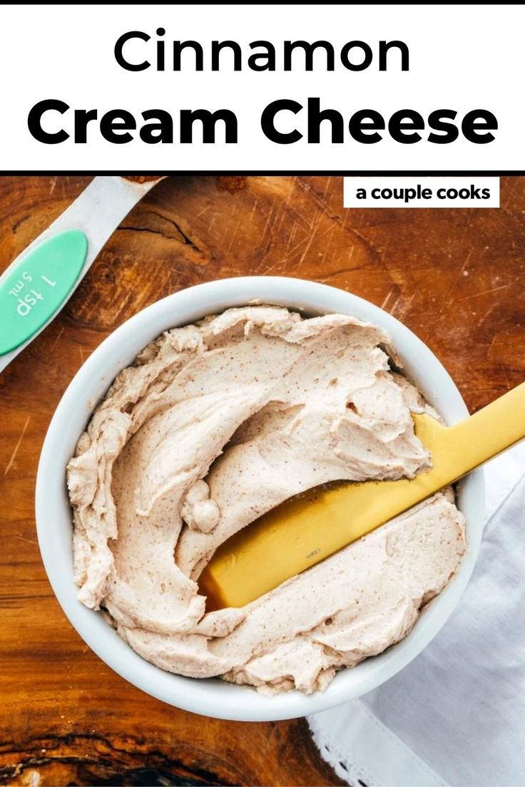 a white bowl filled with cream cheese on top of a wooden table next to a spoon